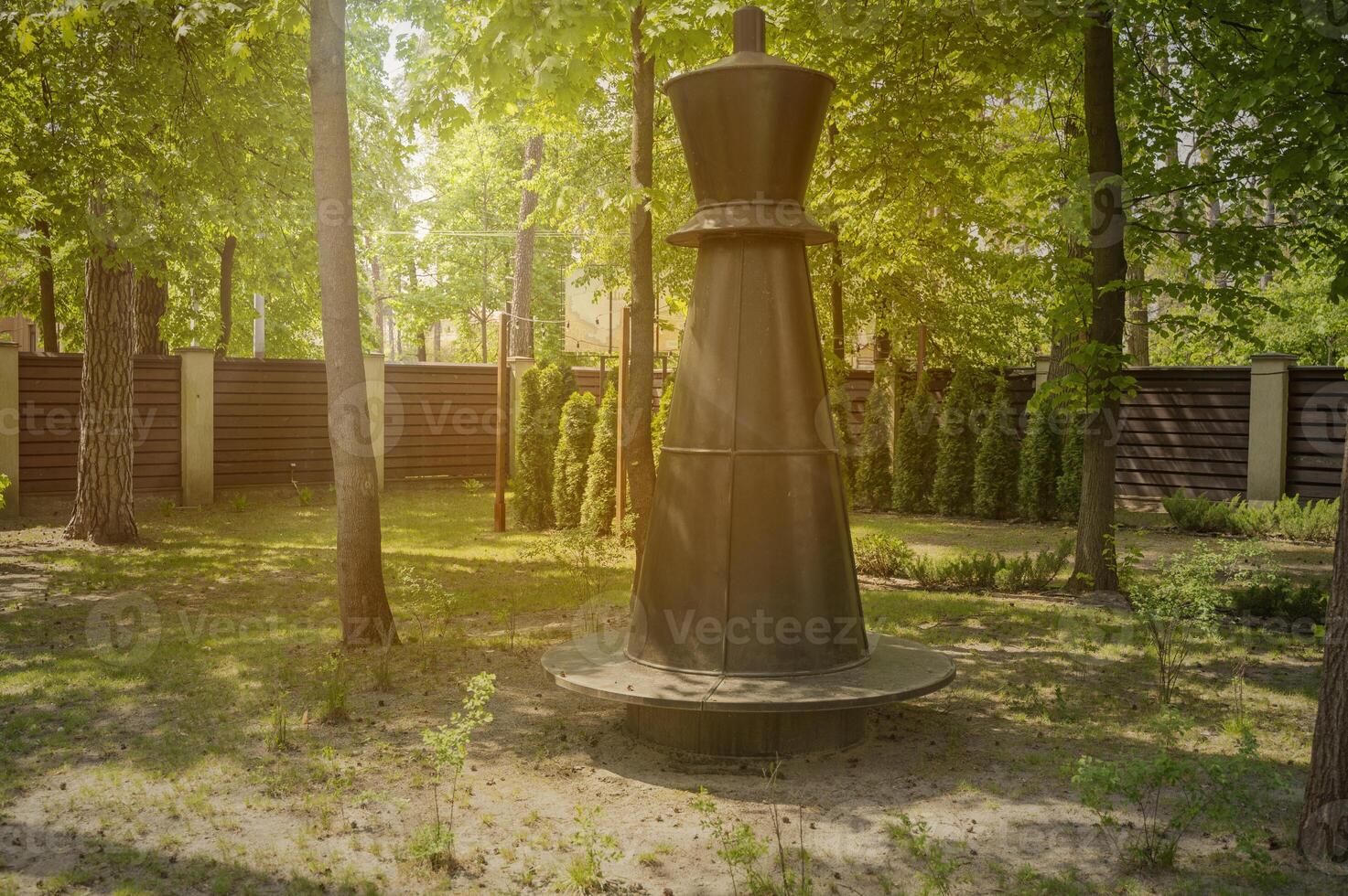 Park bench in the form of a chess piece in the park in the rays of the setting sun. Park with tall trees, green lawn on a sunny day photo