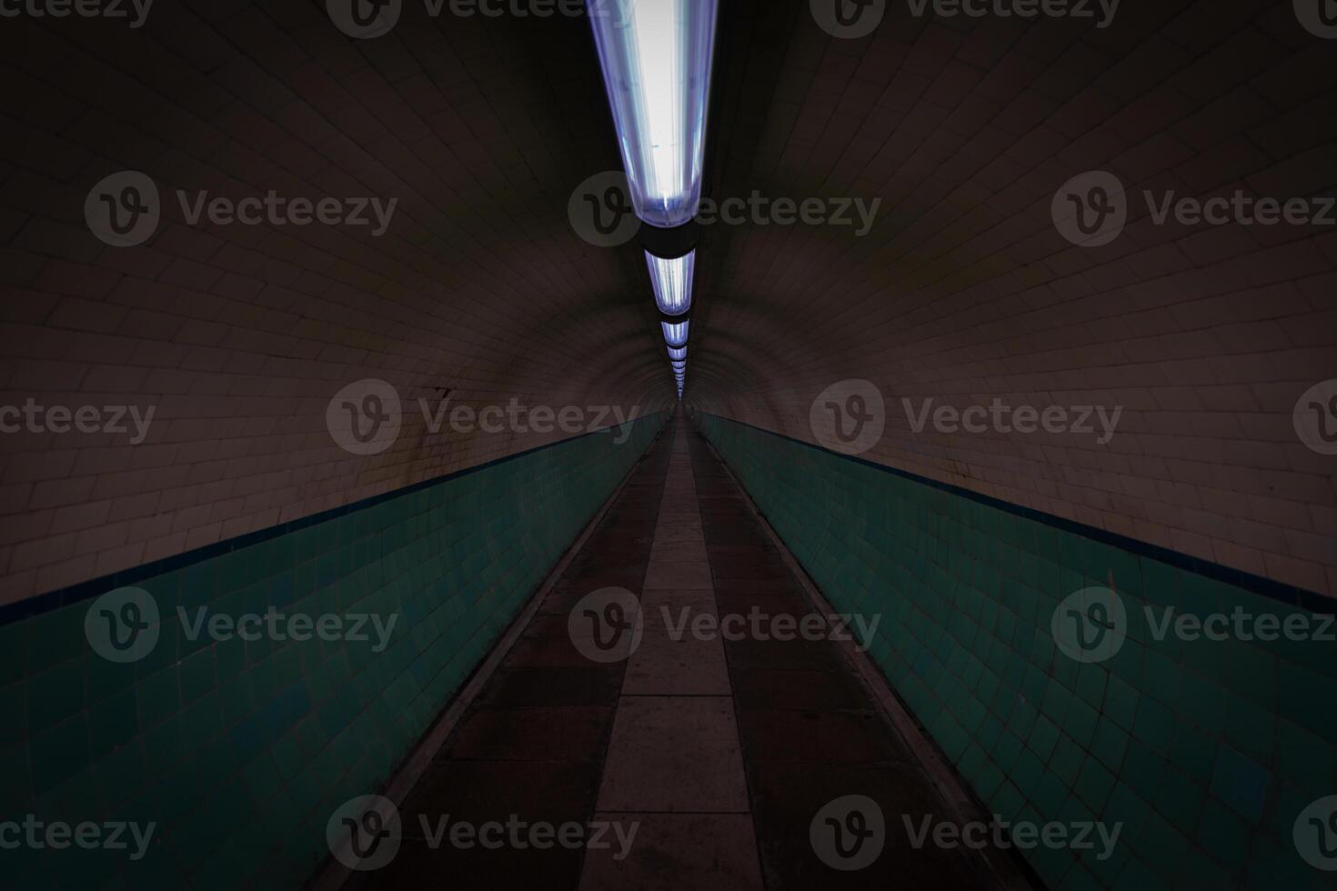 Empty pedestrian tunnel with turquoise tiles and lights illuminating the path photo