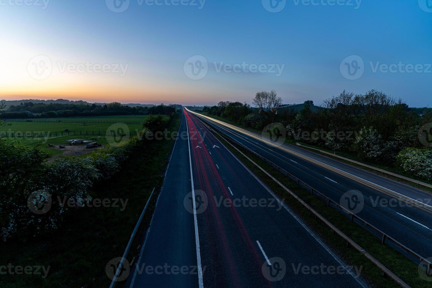 Highway with light trails at dawn illuminating the asphalt near the countryside photo
