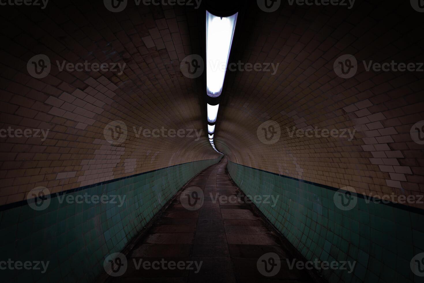 Long illuminated pedestrian tunnel with green tiles and brick walls photo
