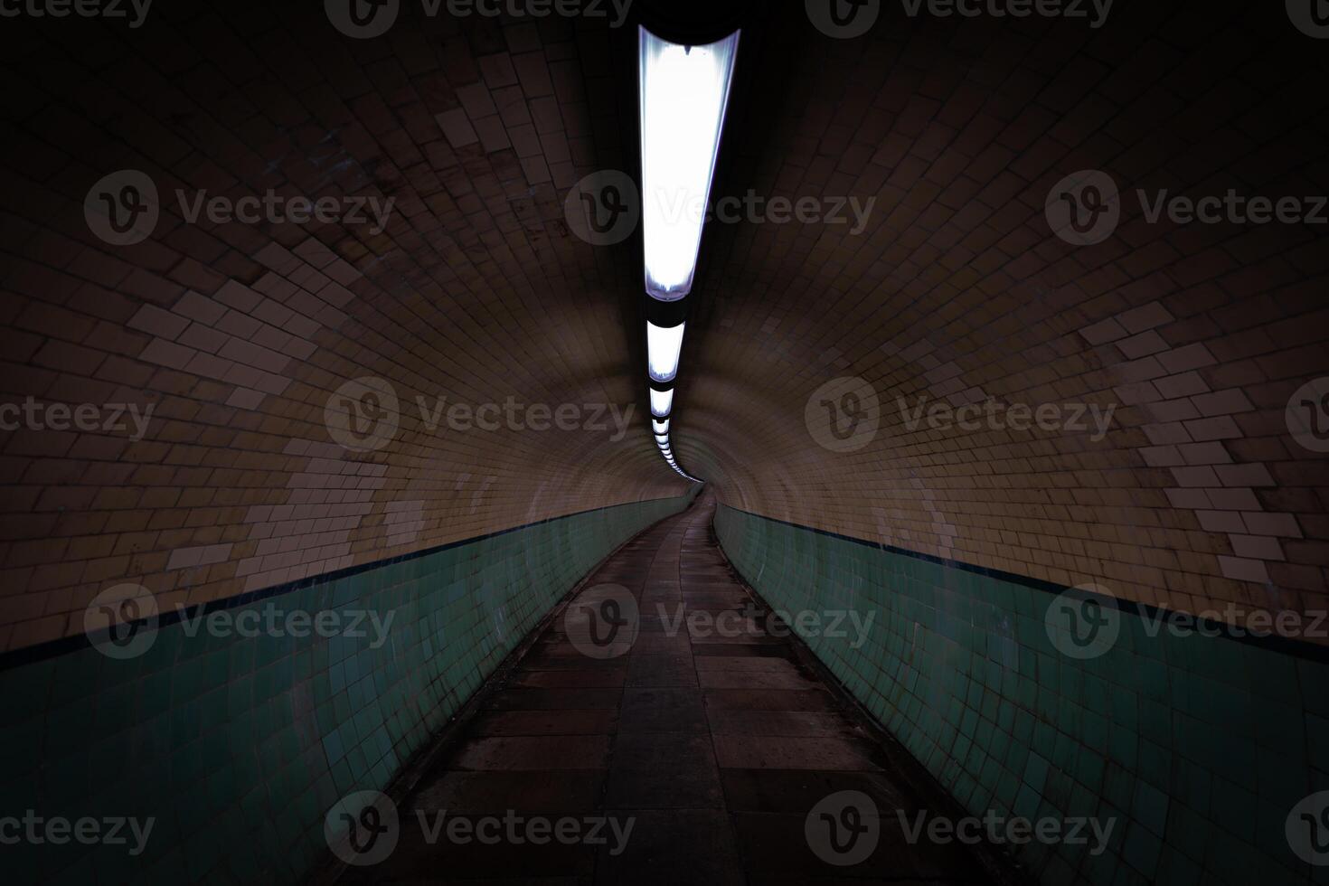 Long, dimly lit tunnel with brick walls and tiled wainscoting photo