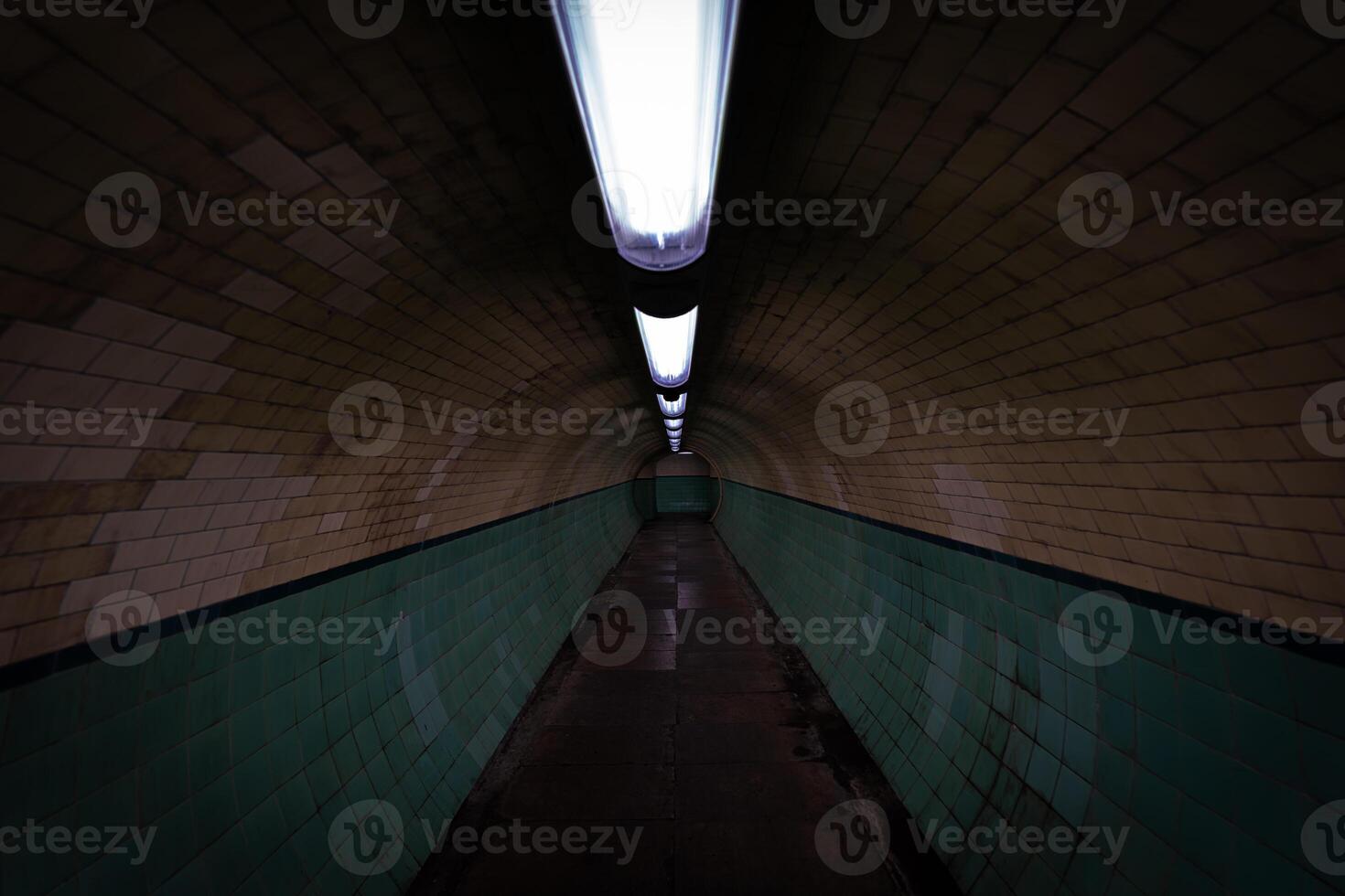 Empty pedestrian tunnel with green tiles and lights illuminating the path photo