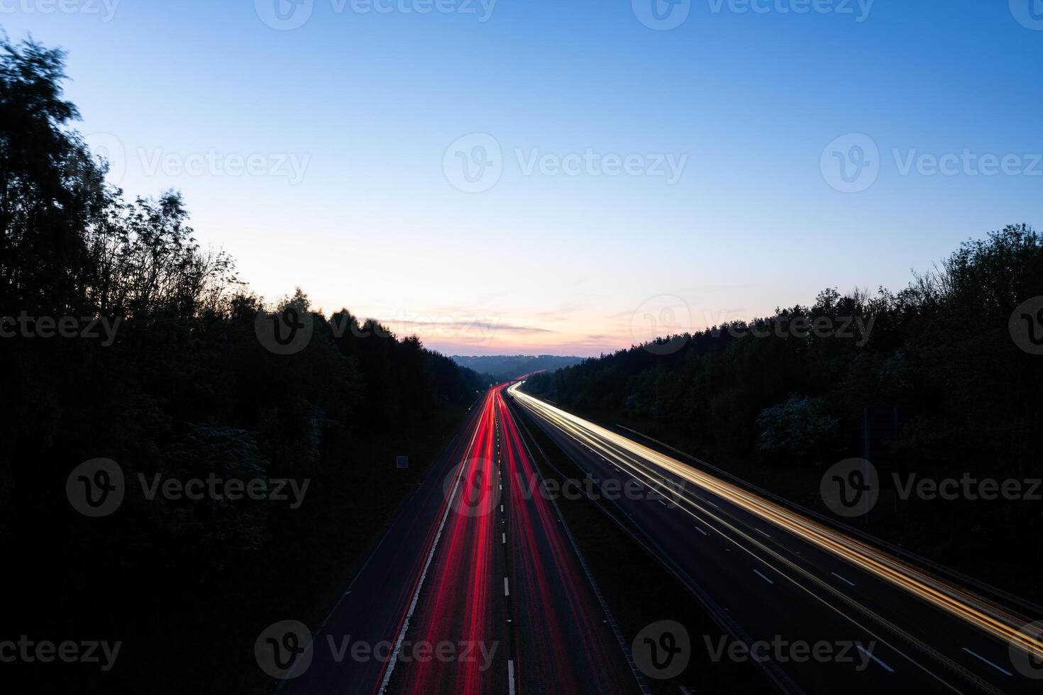 Light trails illuminating highway at dusk between forests photo