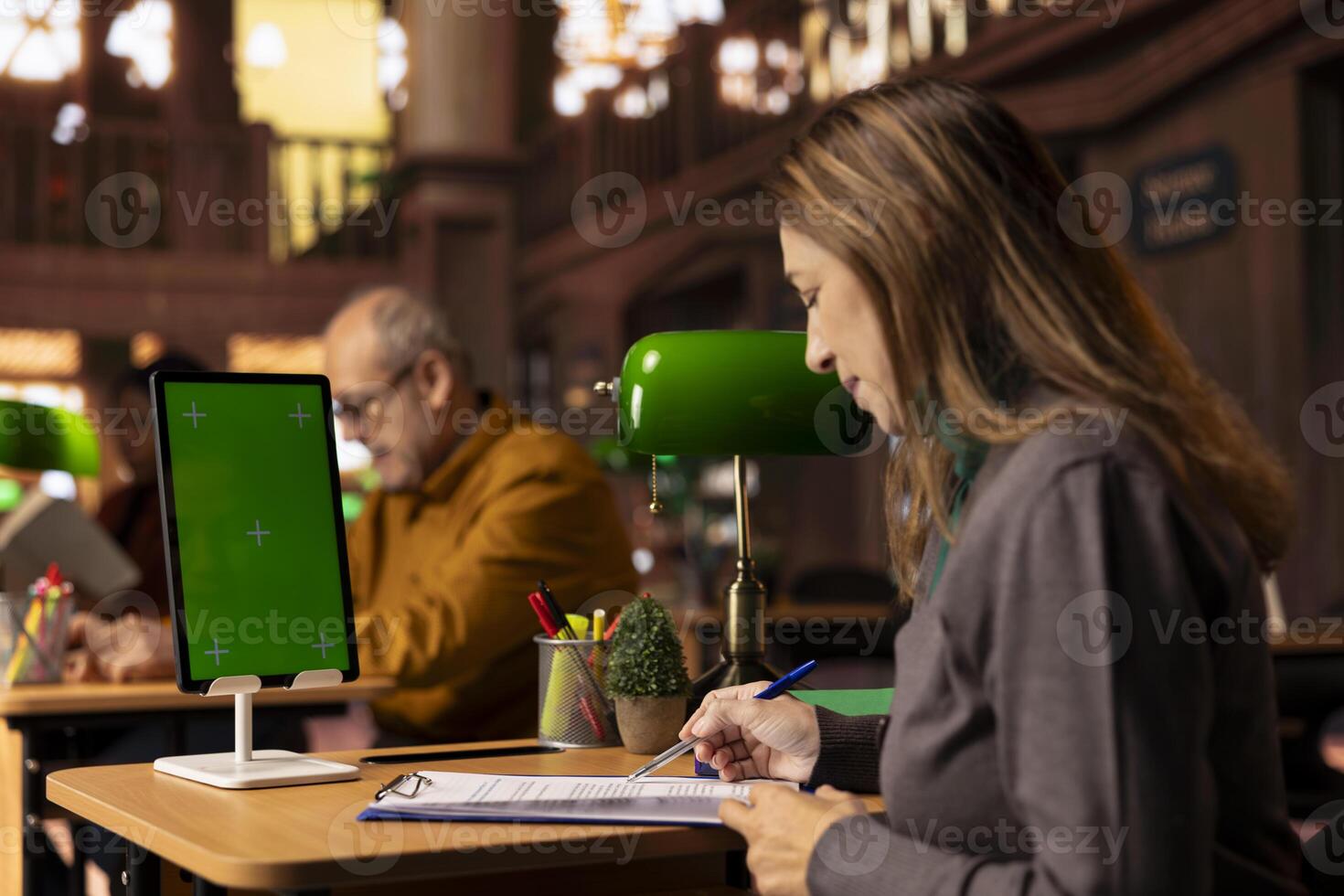 Mature focused student writes a transcript next to copy space display, review academic books and preparing information for her thesis paper in a campus library. Taking notes for research. photo