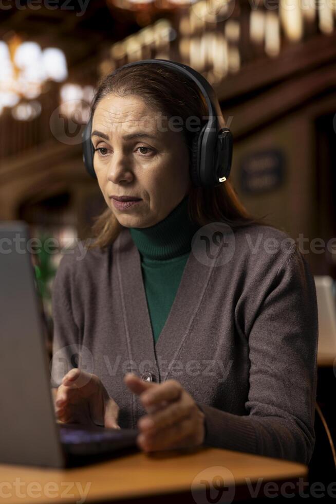 Mature woman in a campus library on a call for a seminar, attending an e learning session that helps with guidance for degree thesis completion. Digital education lesson. photo