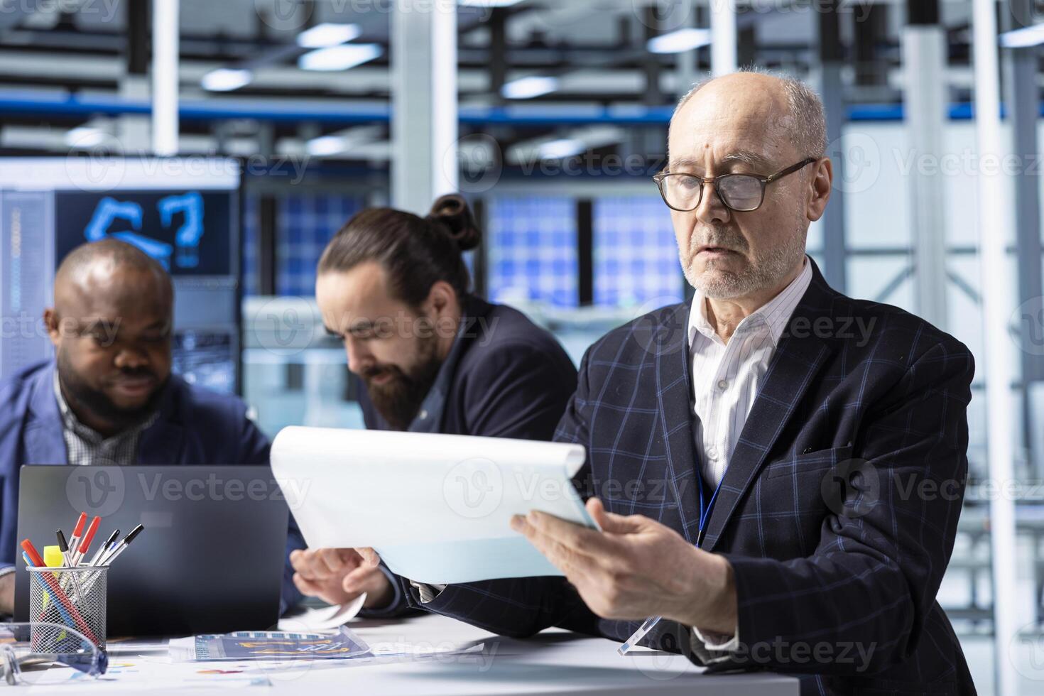 Elderly investor in factory analyzing revenue streams paperwork. Senior industrial plant shareholder looking at documents, factoring in growth scenarios and forecasting returns photo
