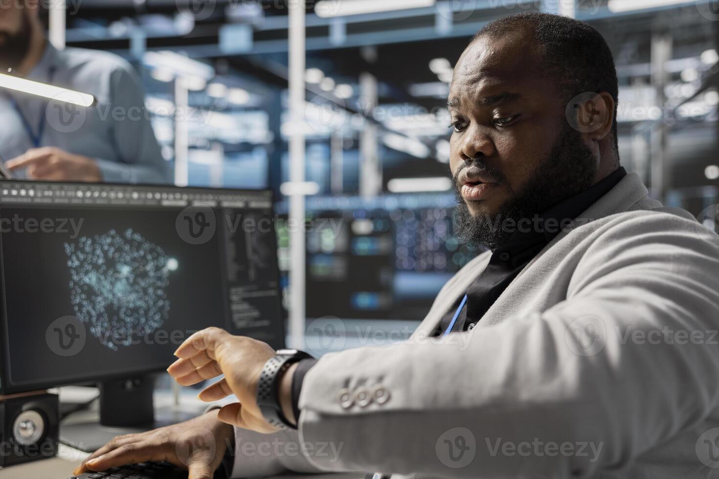 Admin in data center checking time during late shift while working on PC. Server room worker under deadline pressure inspecting settings and verifying final system configurations photo