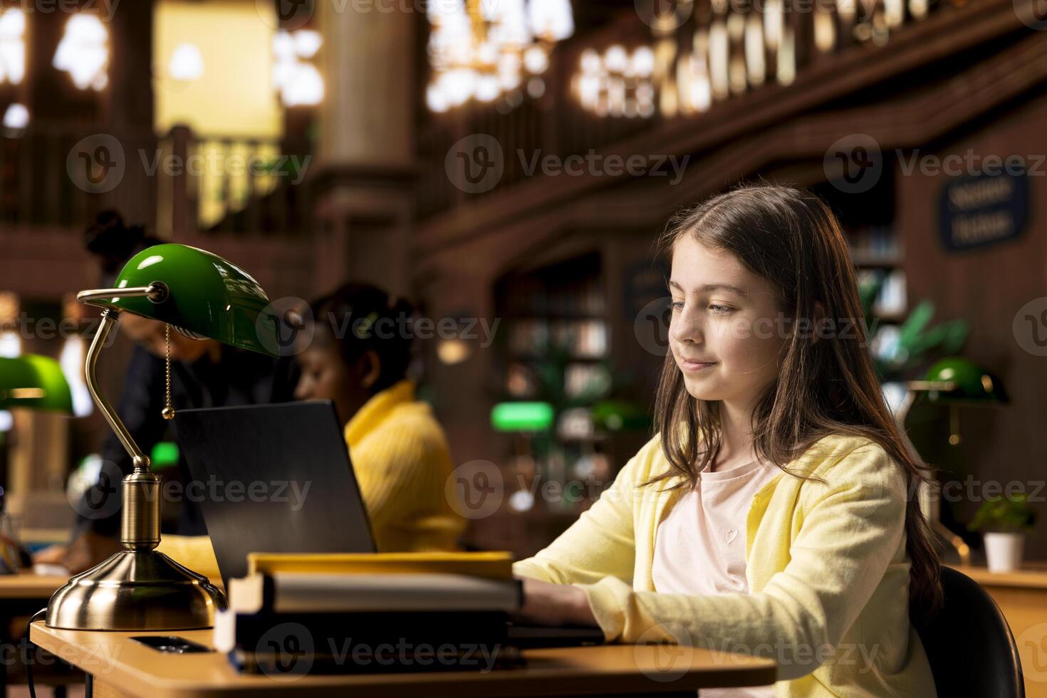 Schoolgirl writing an essay in her laptop using research from library books, completing school assignments and developing her academic skills through study sessions. Educational activities. photo