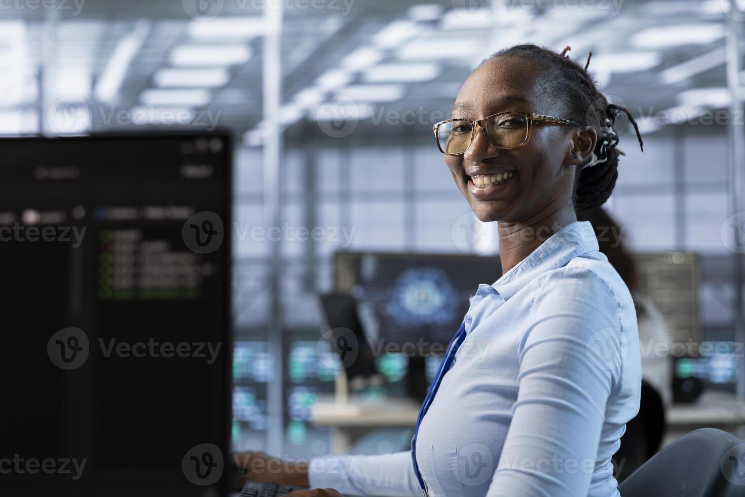 Portrait of cheerful woman tasked with doing checkup on server room rows providing computing resources for different workloads. Joyful admin investigating data center mainframes using PC photo