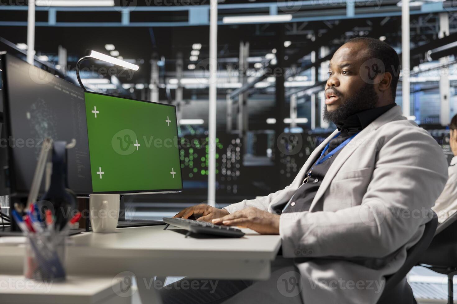 Data center technician inspecting gear using green screen mockup PC, doing maintenance tasks. African american server hub worker using chroma key computer, conducting system checks photo