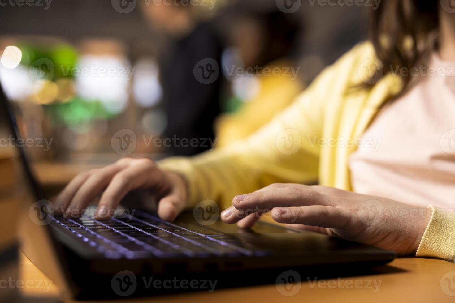 Primary school student sitting at desk in the campus library and writing on laptop, preparing notes and ideas for future lessons. Scholar girl using digital gadget for assignments. Close up. photo