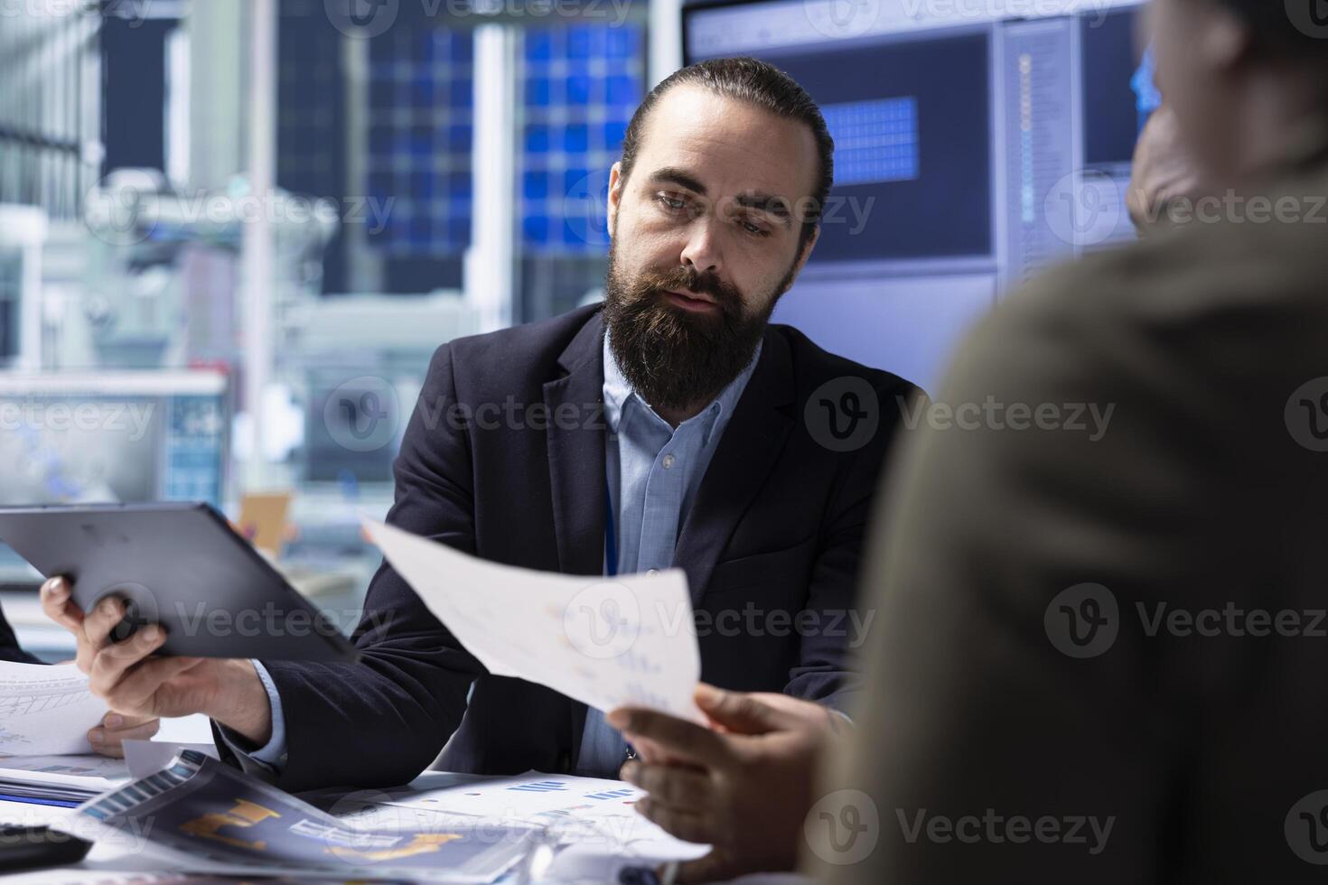 Investors in factory ensuring adherence to industry regulations, looking over paperwork documents. Shareholders ensure following of safety standards before investing, checking documentation files photo
