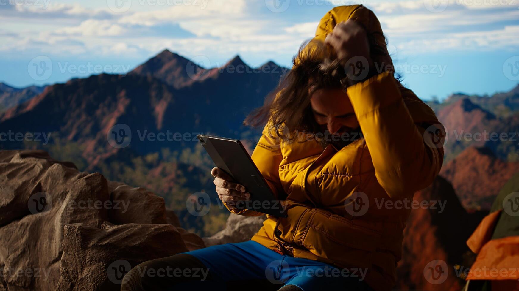 Traveler tries to stay connected in the wilderness but struggles with weak signals, dangerous wind at the top of the mountain. Hiker setting up his tent on a rocky windy peak. Camera A. photo