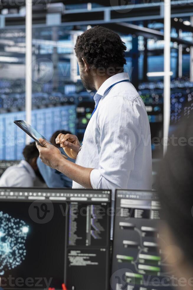 Data center admin uses AI visualization technology on tablet to oversee automated repetitive tasks. Server farm IT professional modifying infrastructure rigs systems based on data analytics graphs photo