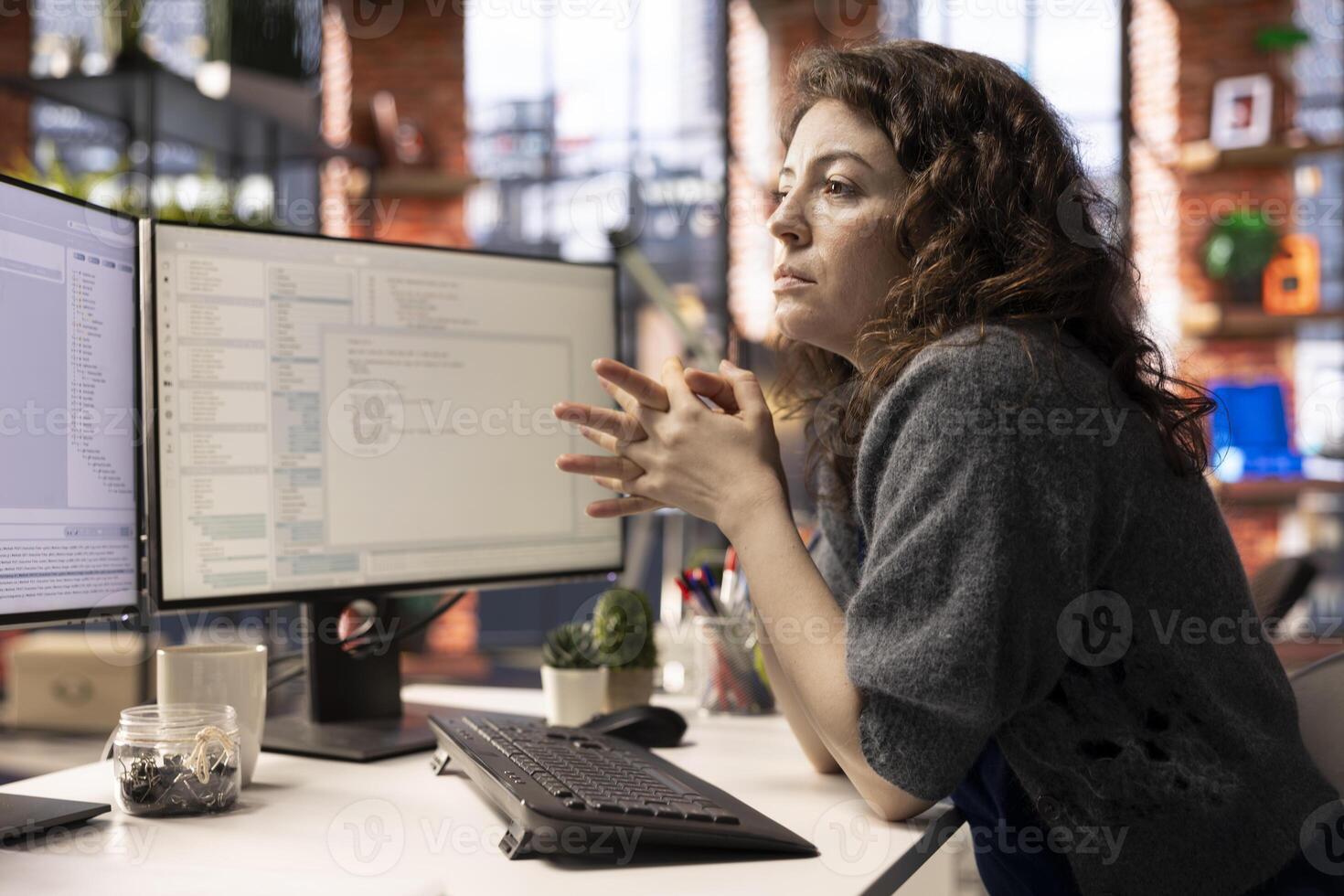 Young woman programming software code on her computer, using coding language for debugging tasks. Workspace with dual monitors helps with software engineering and web development. photo