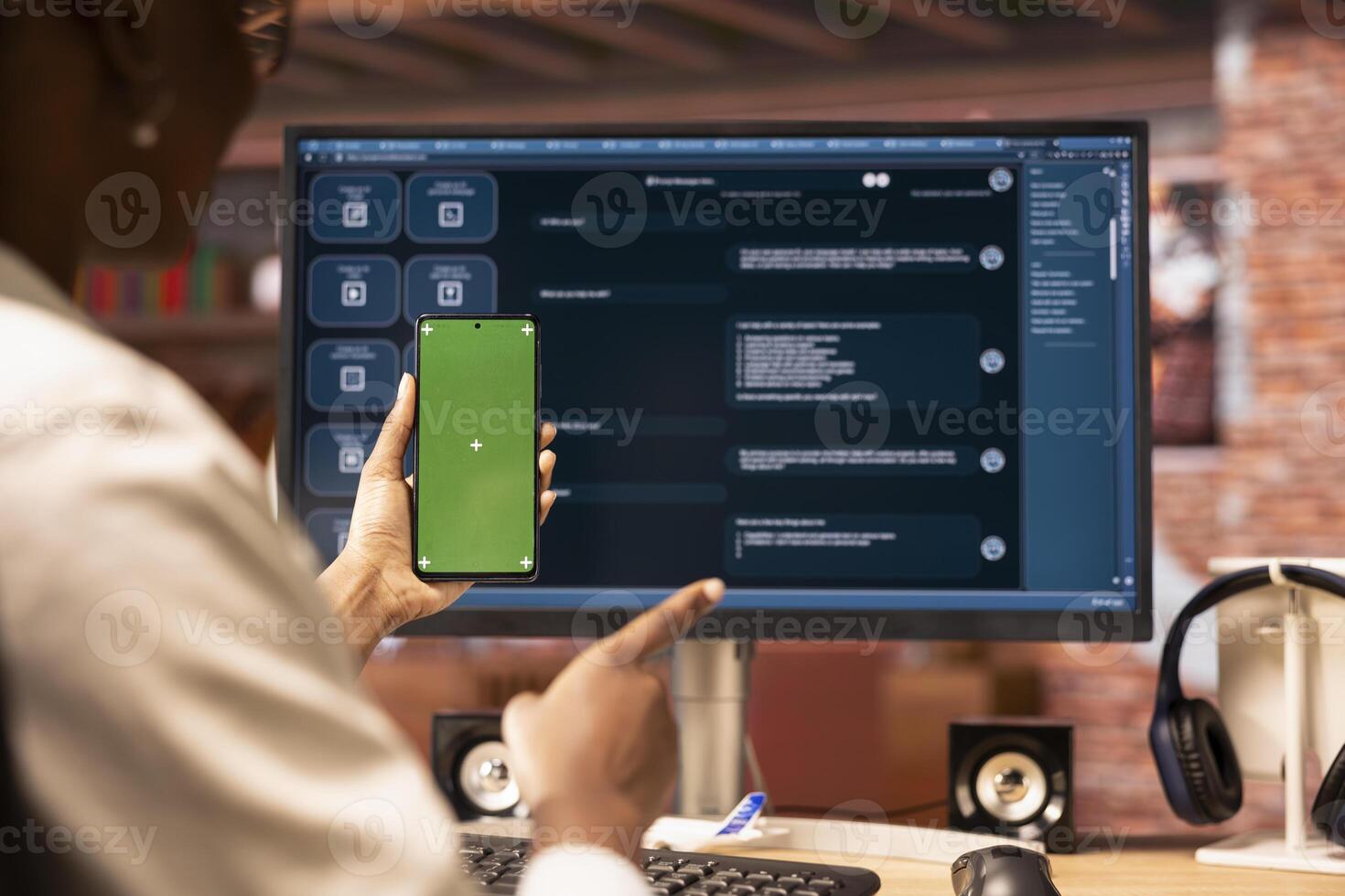 Woman sending vocal commands to AI LLM chatbot on PC using green screen mobile phone. Person speaking in chroma key cellphone to communicate with artificial intelligence chatbot on computer photo
