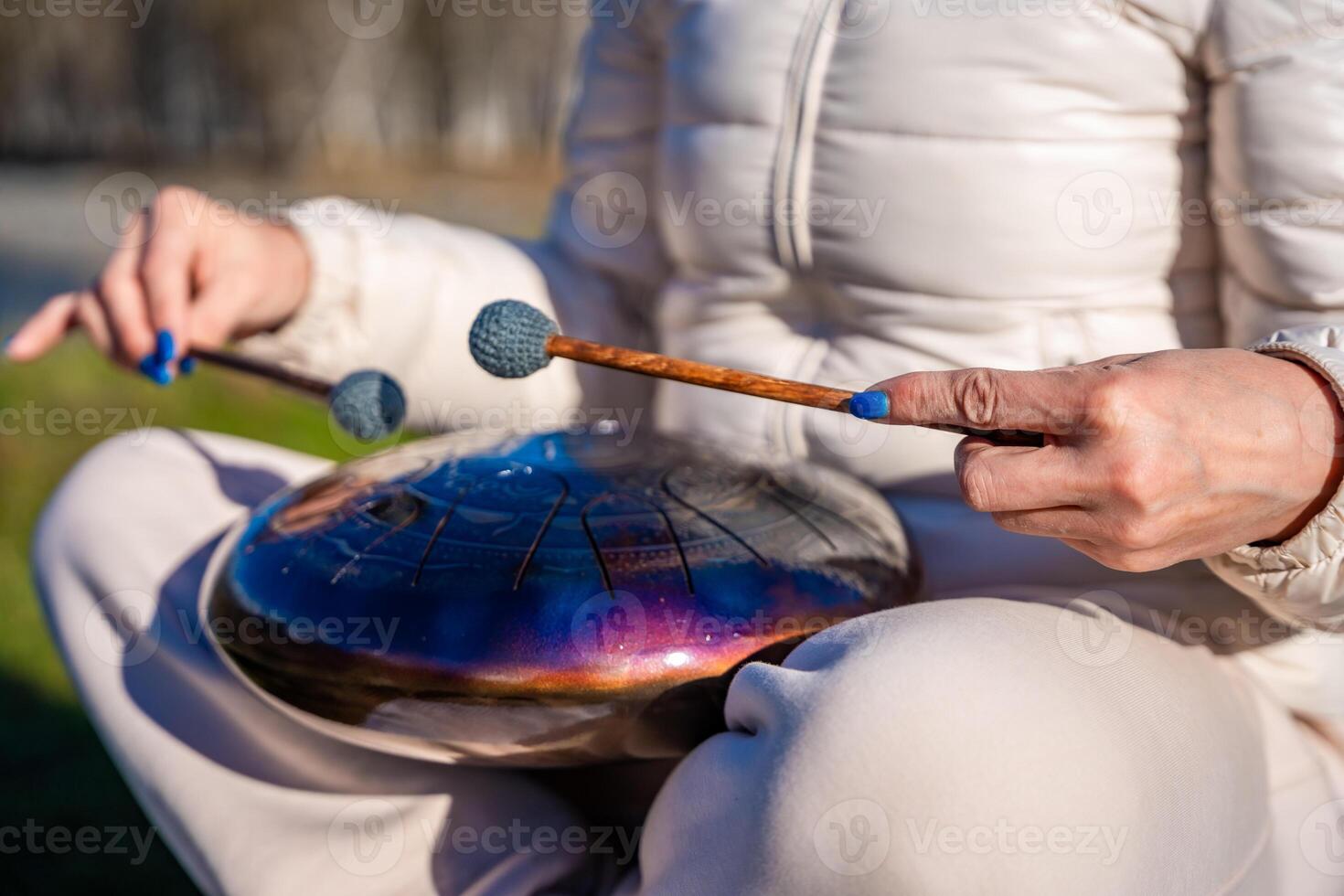 Close-up of hands playing a steel tongue drum with mallets against the backdrop of Altai mountains and river. Concept of sacred sound, touch of nature, and mindful musical ritual. High quality photo