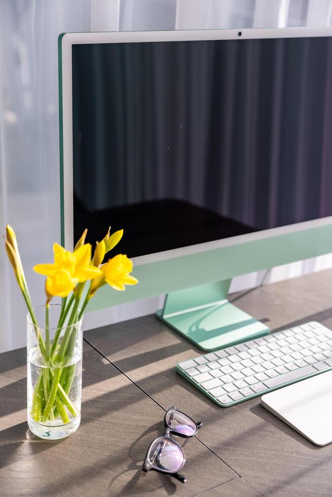 Prague, Czech republic - February 24, 2025. Modern light working space for office or home with green iMac computer, keyboard, glasses and daffodils on the table. High quality photo