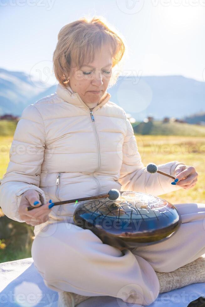 Woman playing a steel tongue drum in nature with a mountain river and Altai landscape in the background. Concept of harmony, mindfulness, and connection with nature. High quality photo