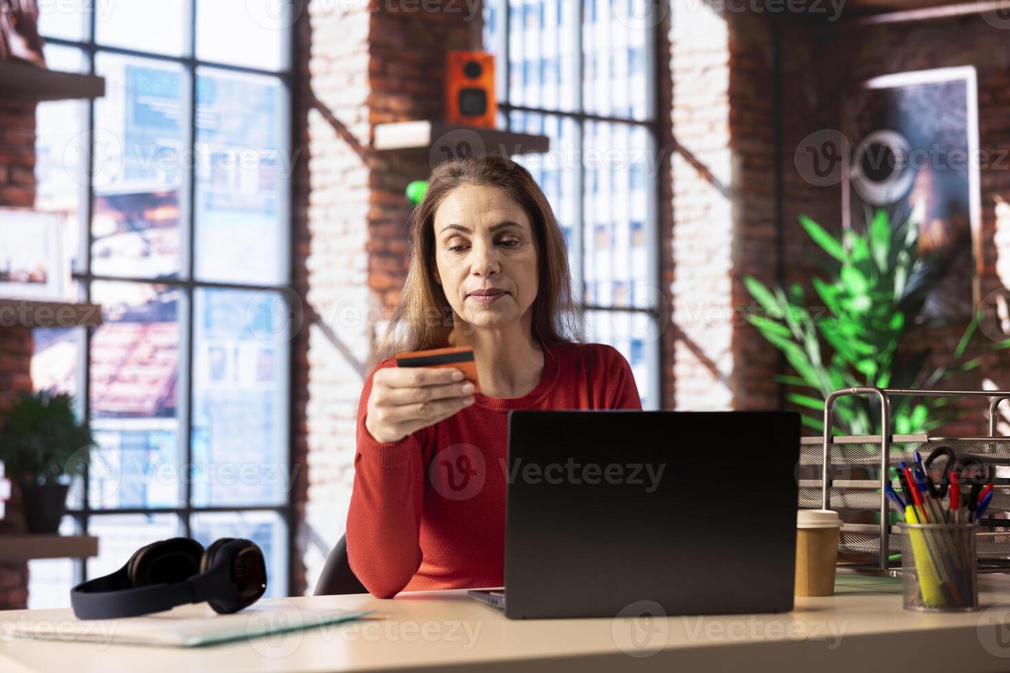 Caucasian adult at home paying for things online on her laptop, entering credit card numbers to confirm a transaction and make purchase by placing the order. Online shopping in her loft. photo