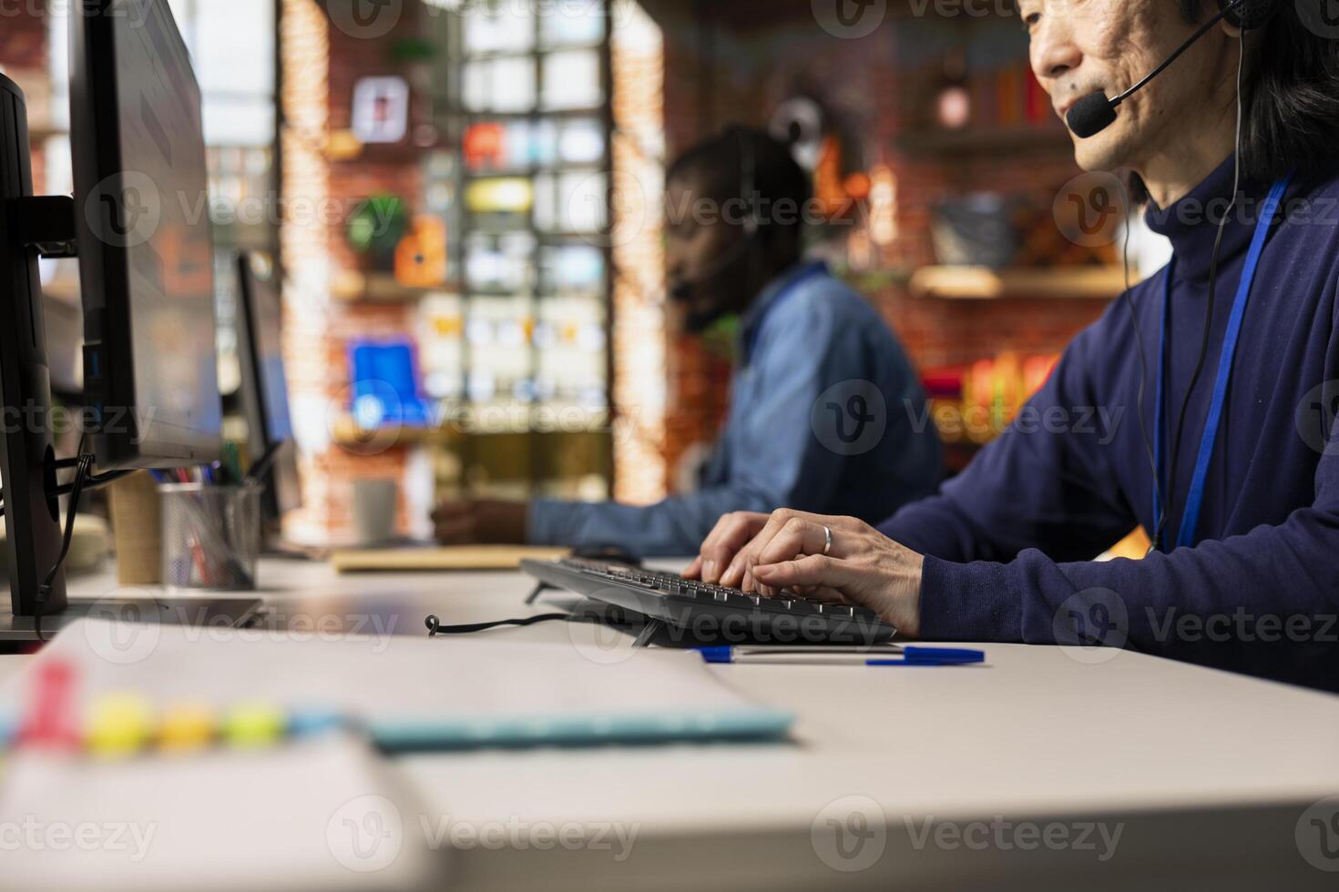 Call center agent talking in headset mic, typing on keyboard, providing step by step guidance to customer. Customer center employee at PC desk, walking clients through technical solutions photo