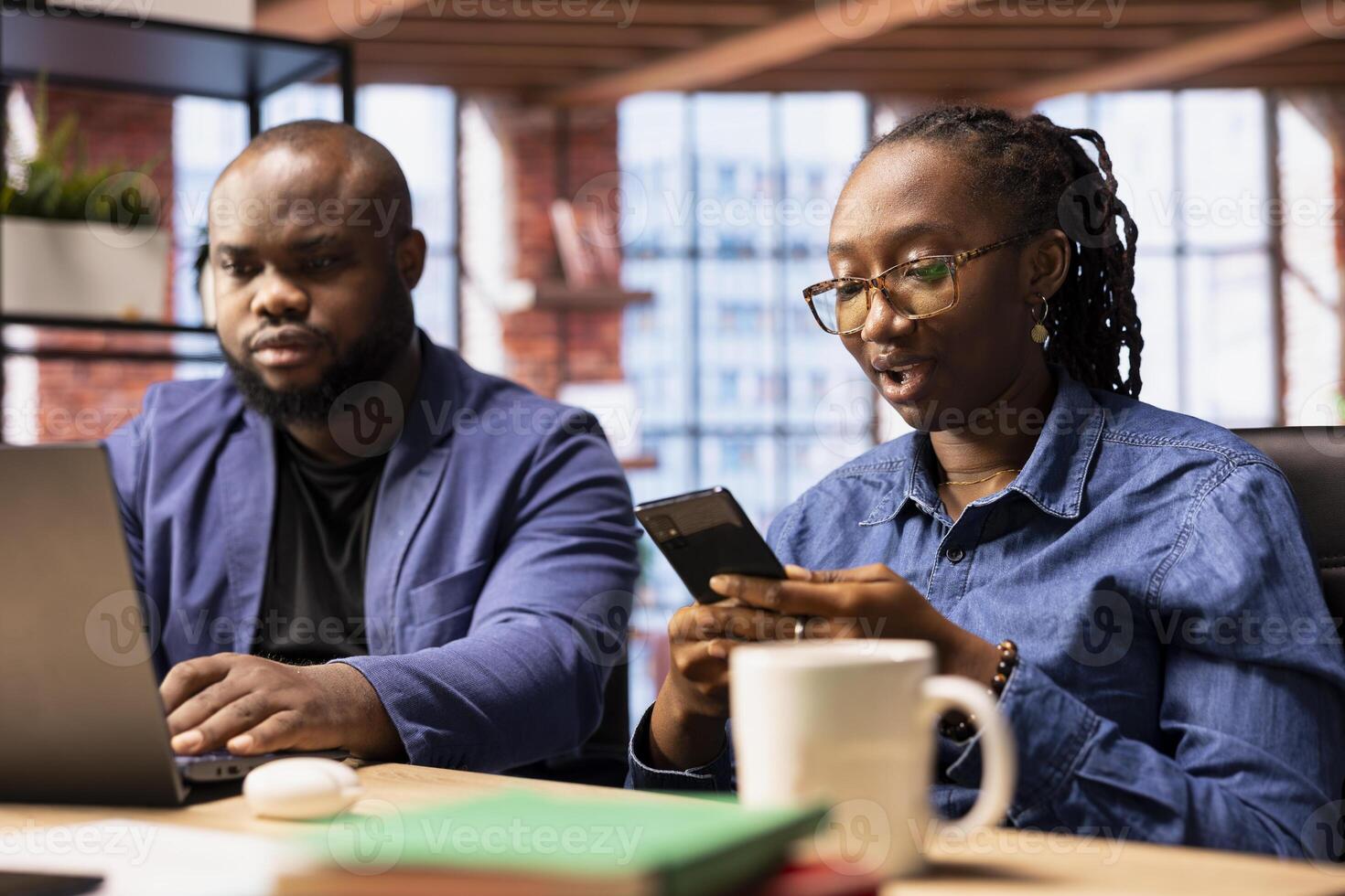African American freelancers at home collaborating on a research project, man using online reports and analytics via laptop. Young woman manages web correspondence on mobile phone. photo