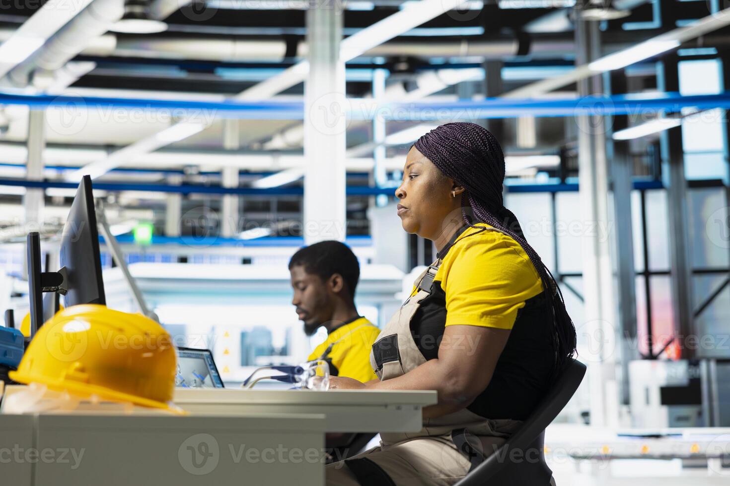 Technician monitors manufacturing data on pc in solar panel factory, employee finetunes equipment settings to support efficient solar power production. Woman seated next to assembly line. photo