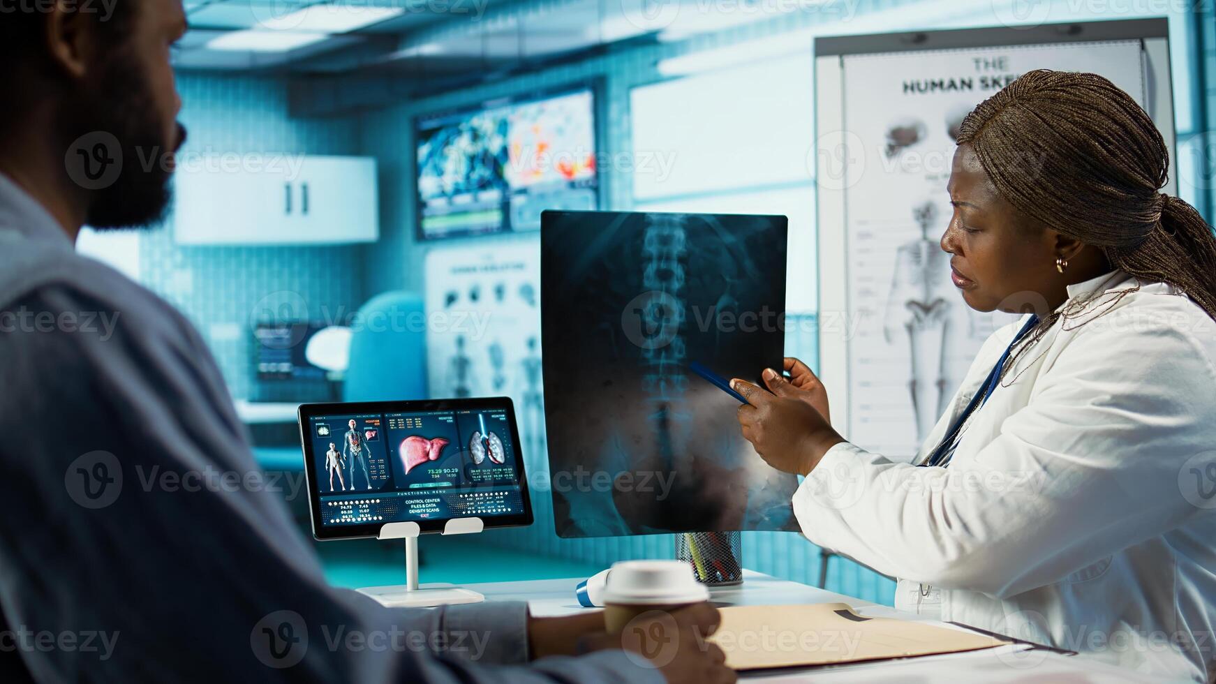 Medical professional explaining the x ray imaging for a diagnosis, doing scan interpretation during check up visit. African american female medic gives feedback to male client. Camera B. photo