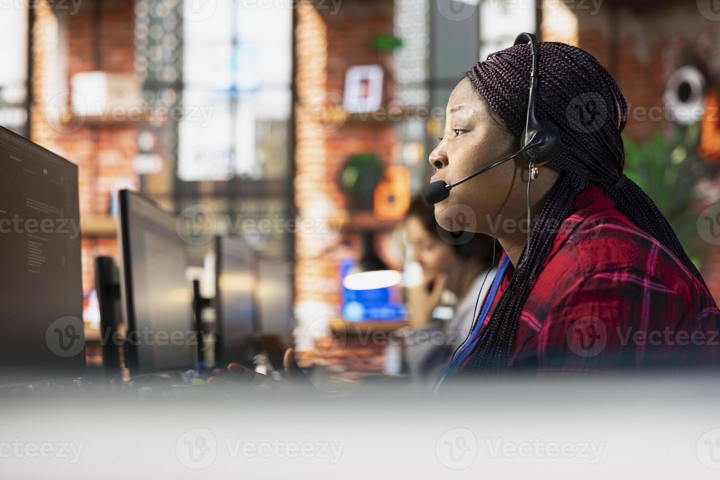 Call center representative in office helping customers by answering questions, close up shot. African american woman in customer support workspace using headset to talk with clients photo
