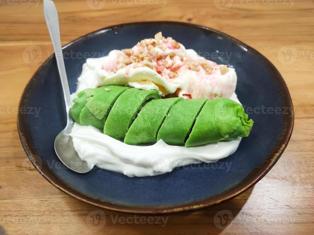 Es Pisang Ijo, a typical dessert from Makassar, Indonesia. A dish of bananas wrapped in green dough, served with sumsum porridge, red syrup, ice cream and roasted peanuts. photo
