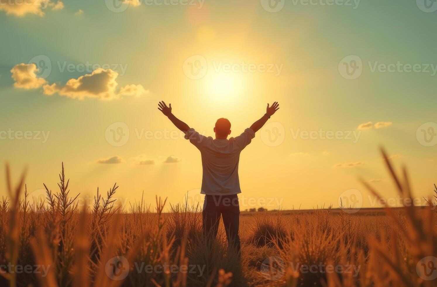 A person stands in a golden field with arms raised towards the rising sun during early morning light on a clear day photo