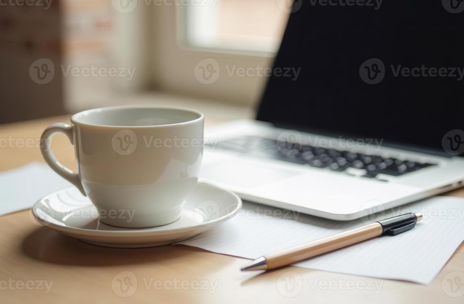 A cozy workspace featuring a cup of coffee on a wooden desk beside a laptop and documents during a sunny morning photo