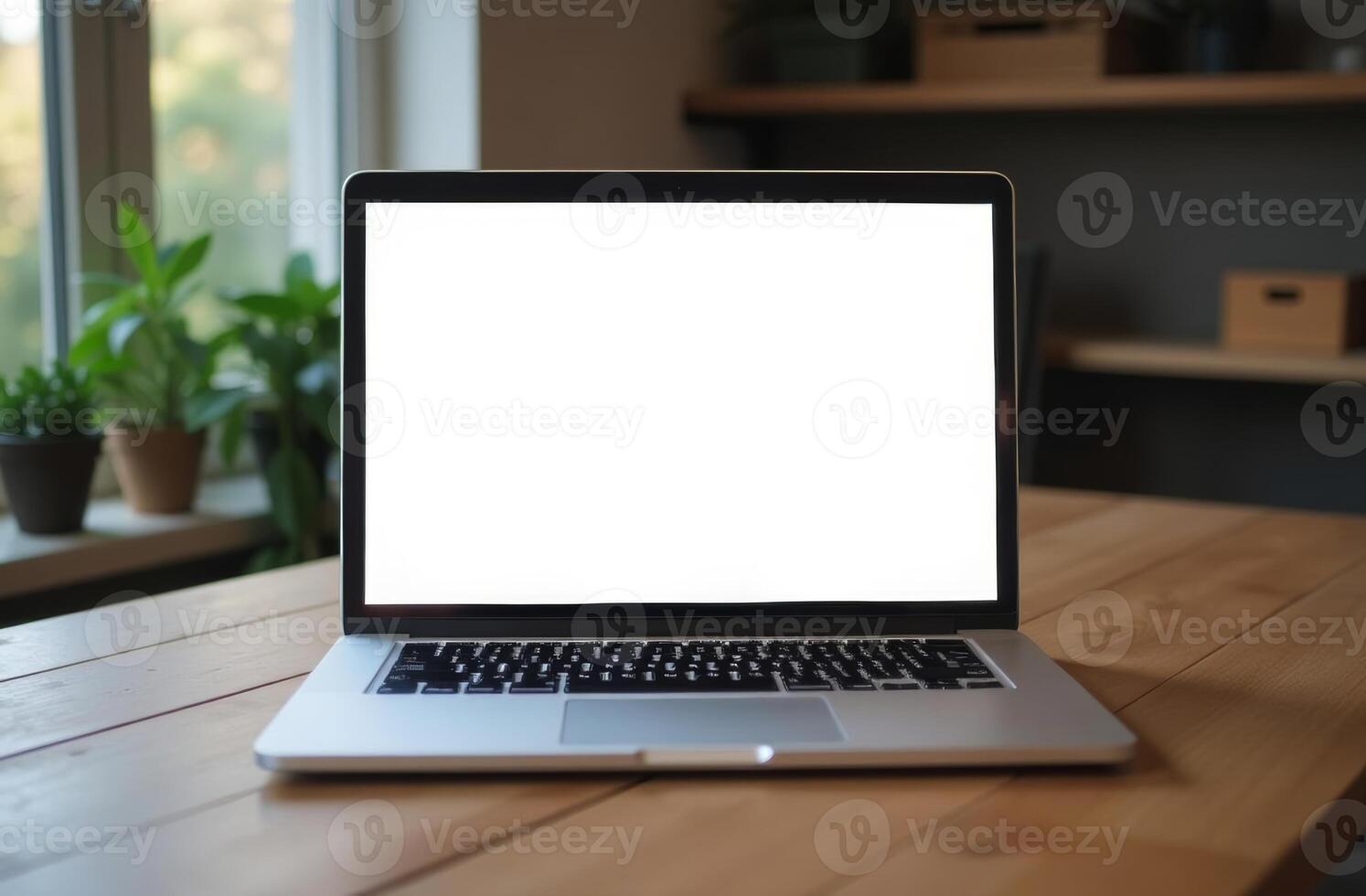 A blank laptop screen on a wooden table with plants in the background during daylight in a cozy indoor workspace photo