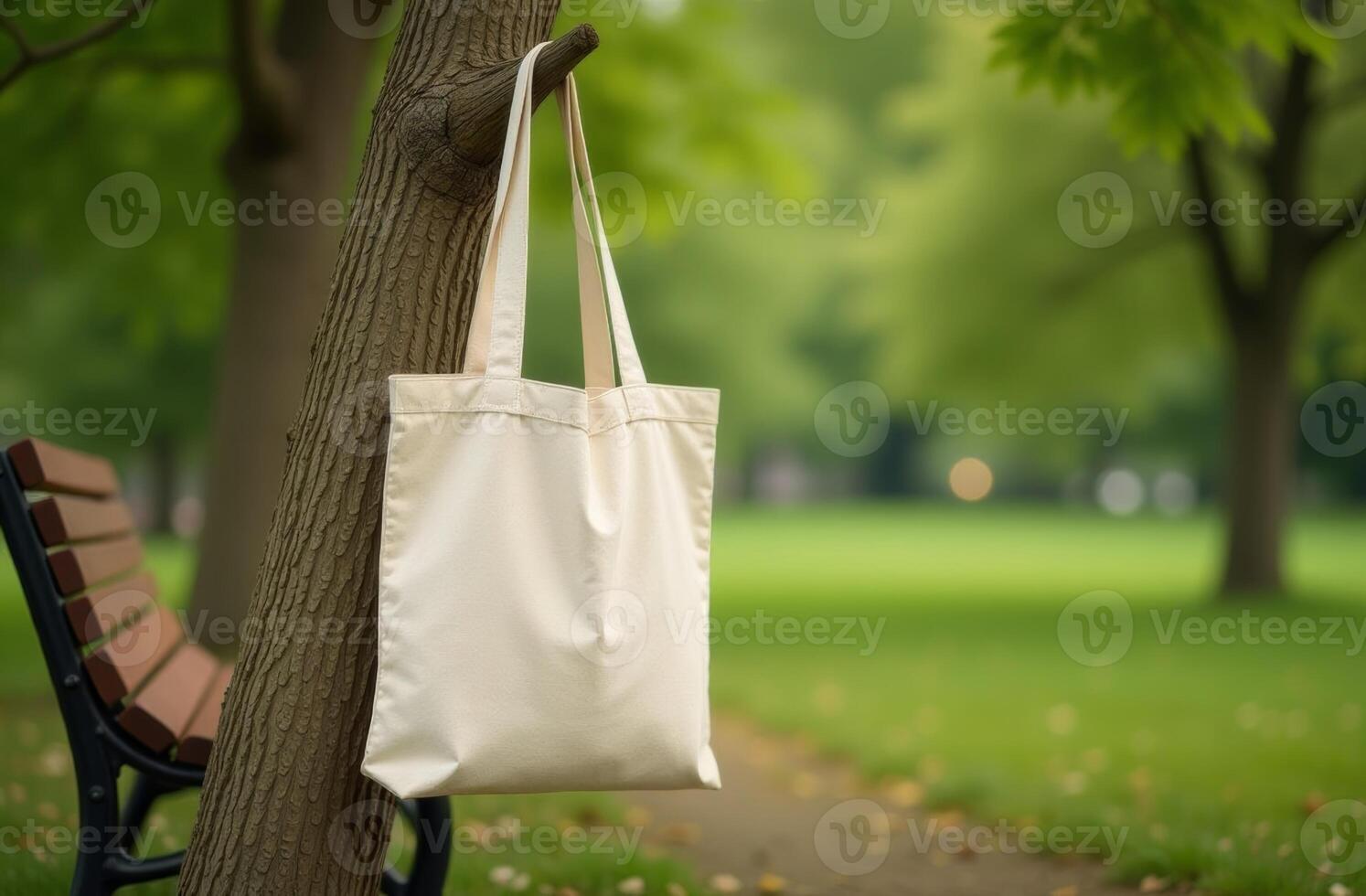 A canvas tote bag hanging from a tree branch in a peaceful park setting during a sunny day photo
