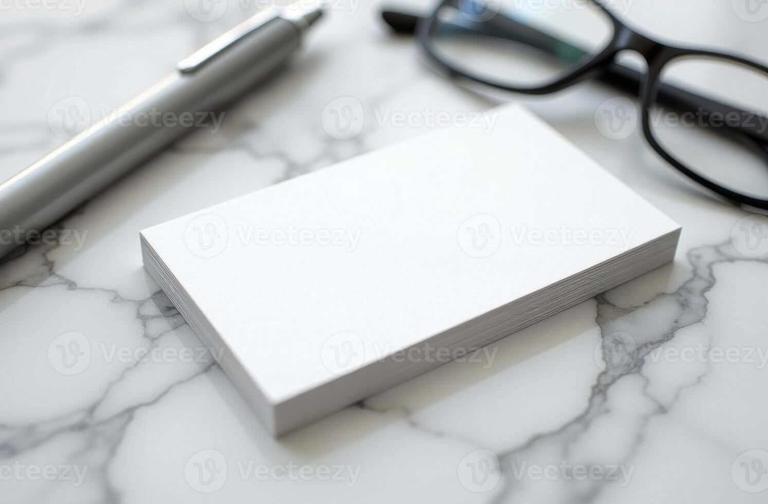 Blank business cards placed on a marble surface alongside a pen and reading glasses in a well-lit environment photo