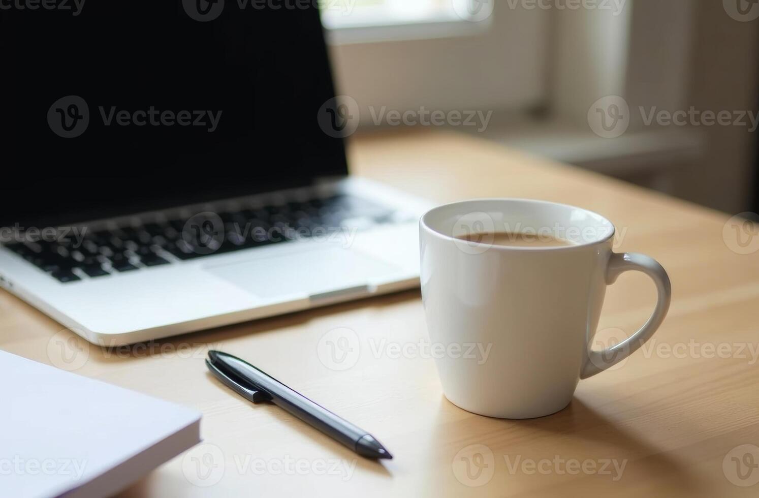 A steaming cup of coffee sits beside a laptop on a wooden desk, creating a cozy workspace atmosphere in natural light photo