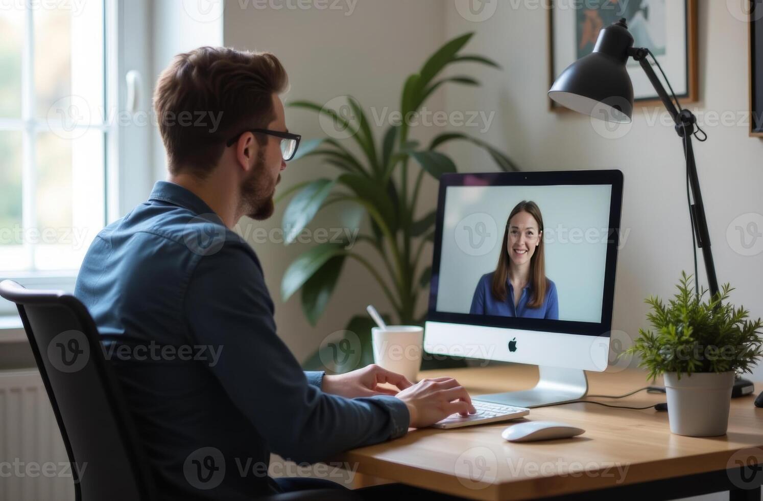 Man working at a desk and chatting with a woman on a computer during daylight in a cozy home office photo