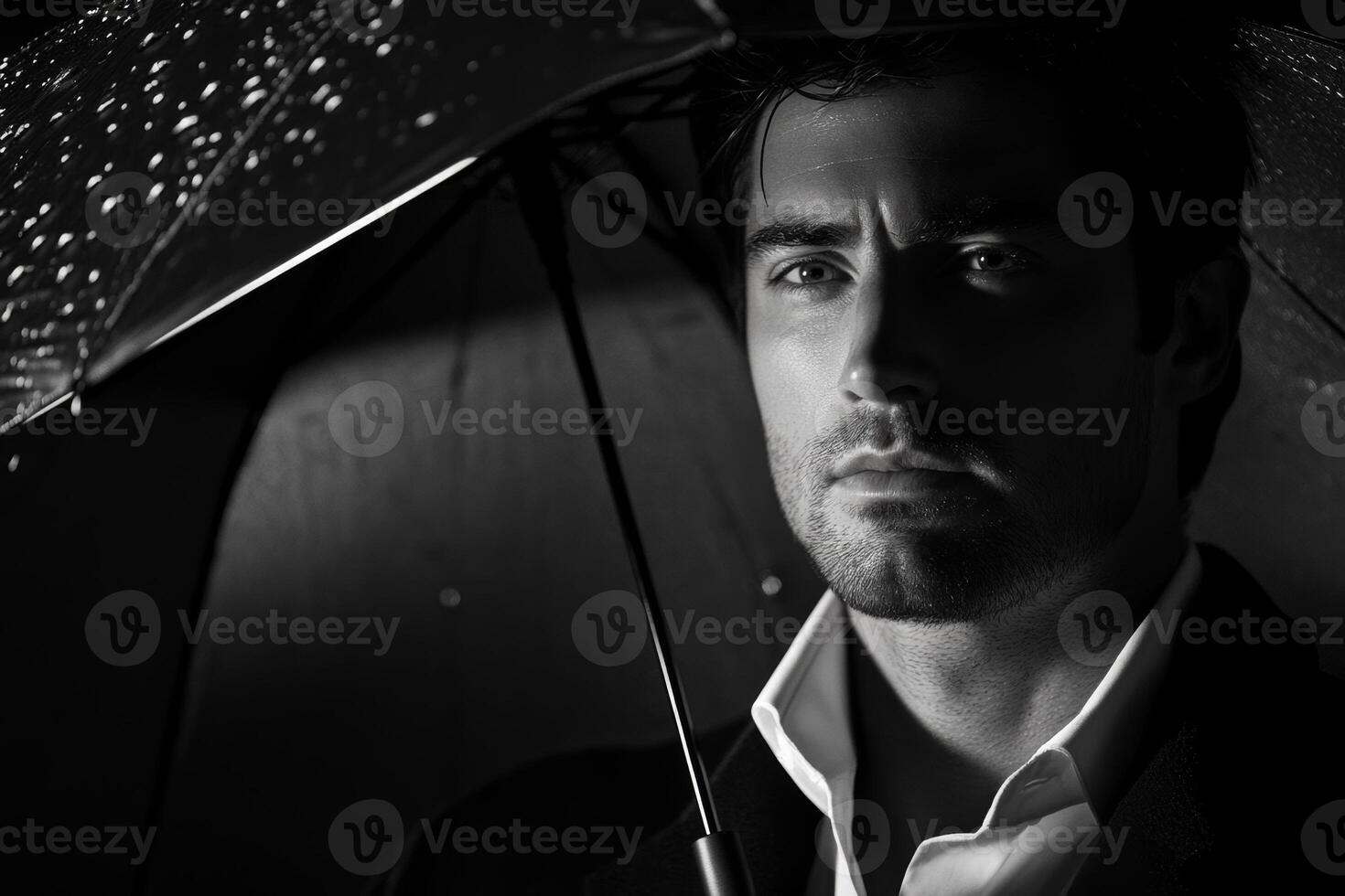 Man under umbrella in rain with serious expression during nighttime in urban setting photo