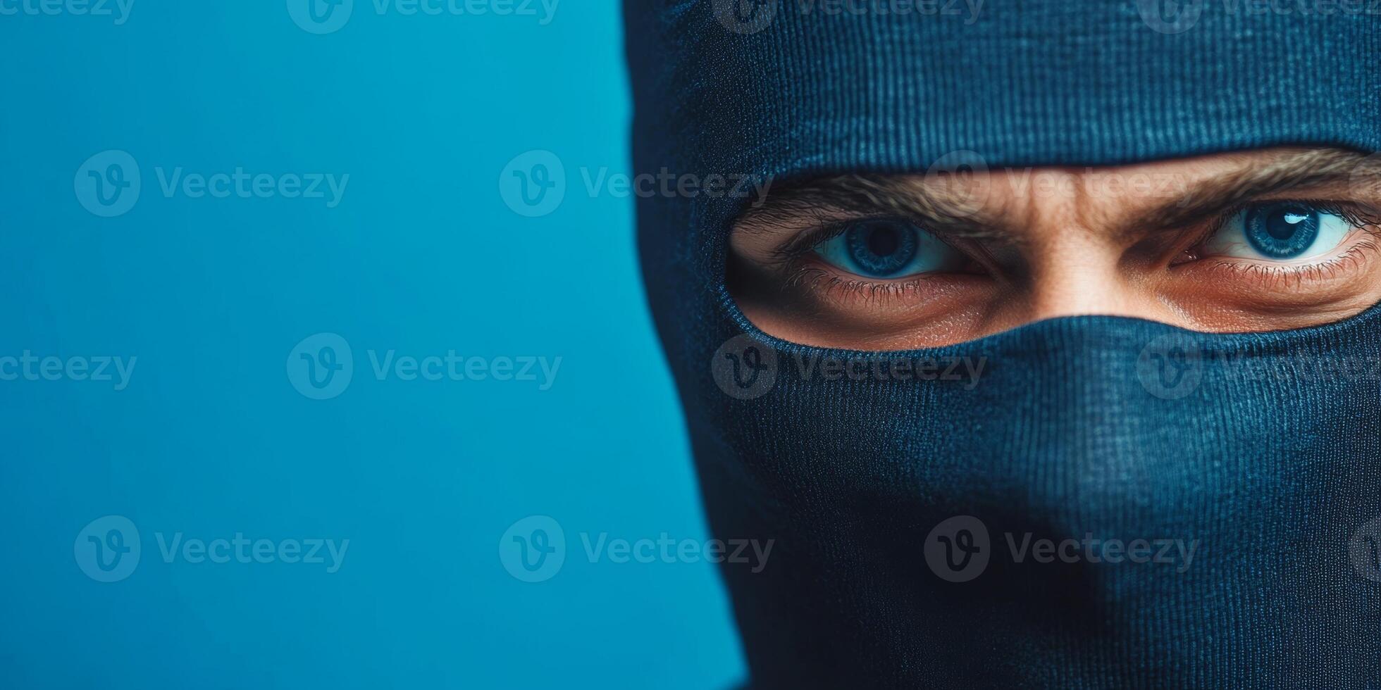 Masked individual with striking blue eyes posing against a simple blue backdrop during an intense moment of secrecy photo