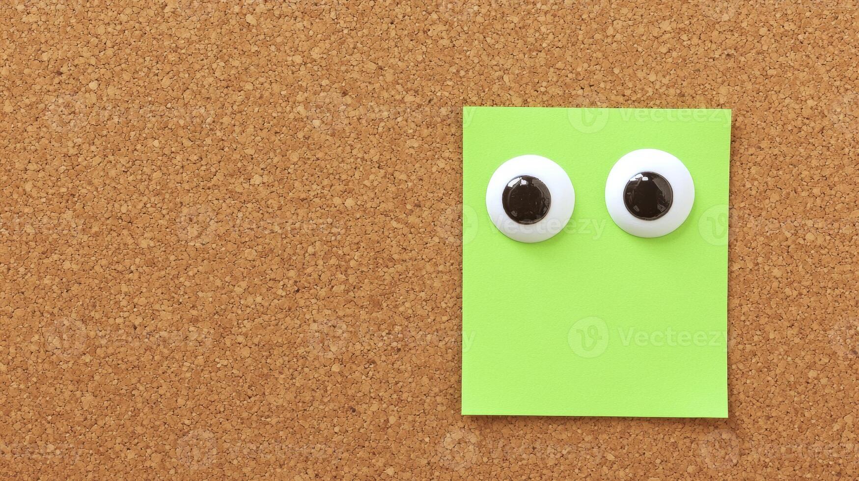 Fun and creative green sticky note with googly eyes on a corkboard background photo