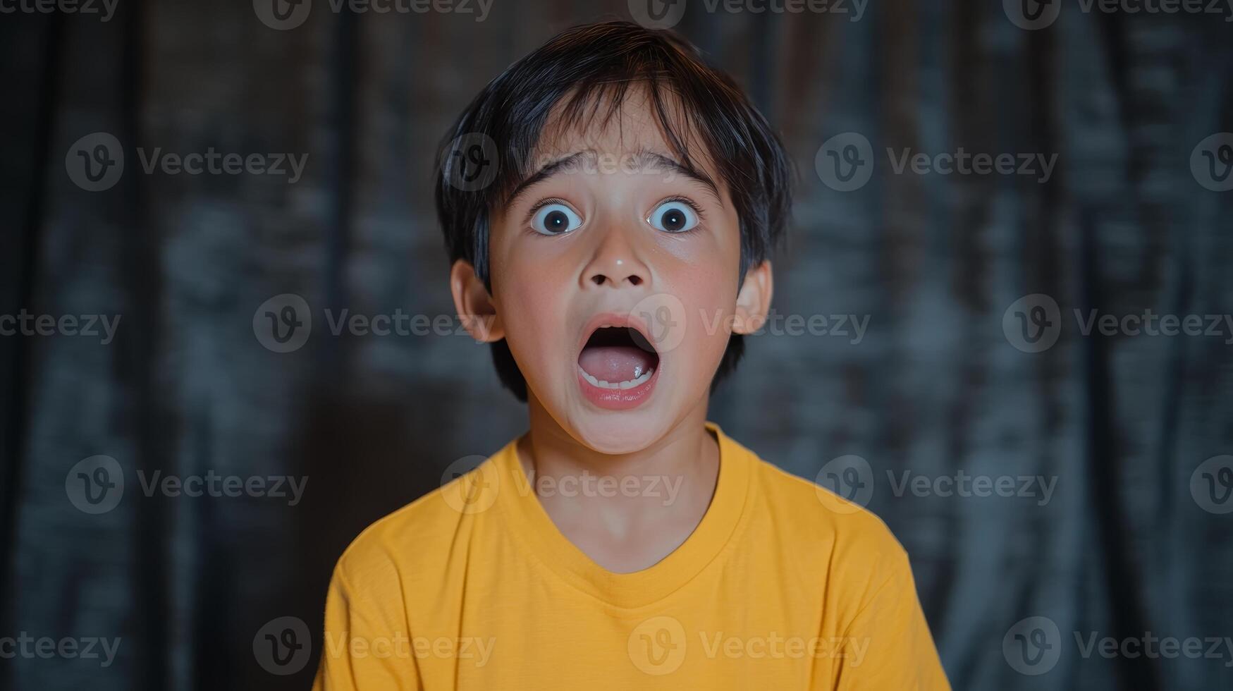 Child shows extreme surprise or fear in indoor setting with dark background while wearing a yellow shirt photo