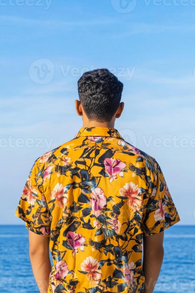 Man in a floral shirt stands by the ocean gazing at the serene horizon on a sunny day photo