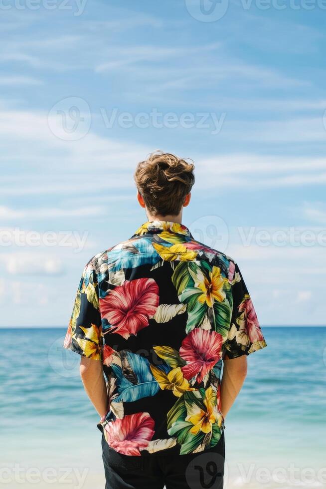 Man in tropical shirt enjoys a serene beach view as waves gently lap the shore under a bright sky photo