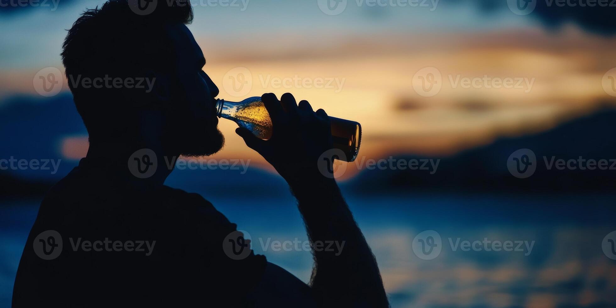 Enjoying a refreshing drink at sunset by the water while silhouetted against a colorful sky photo