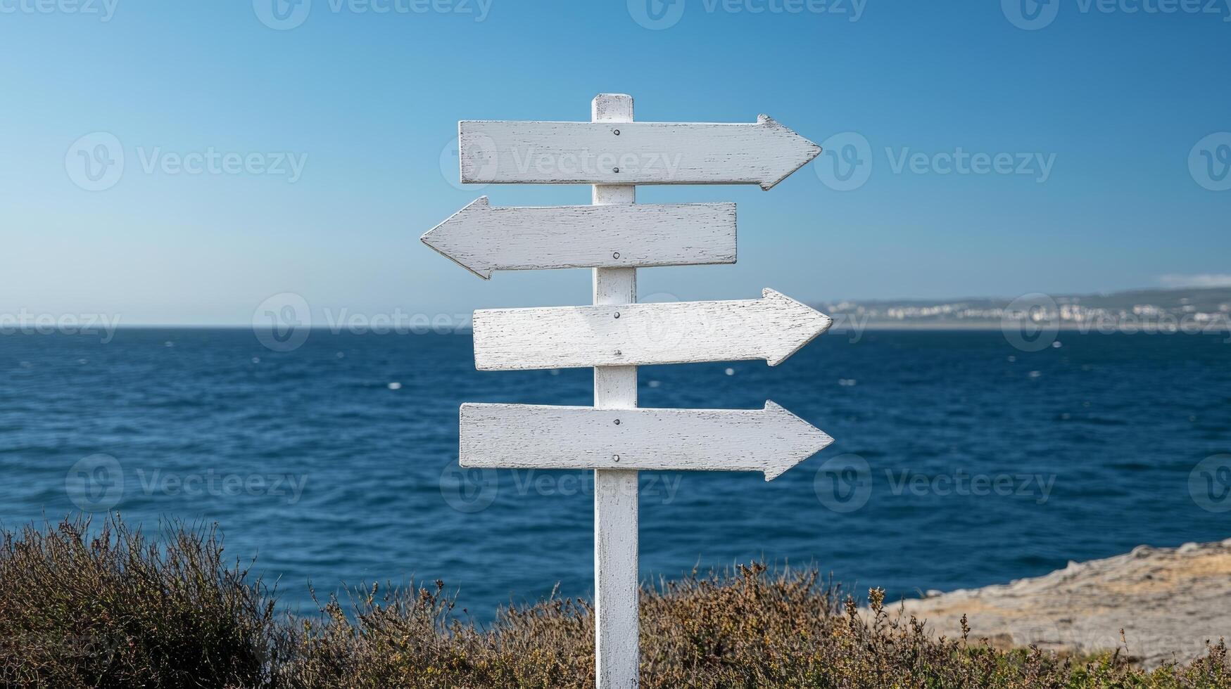 Coastal signpost with multiple directions near serene blue water on a clear day photo