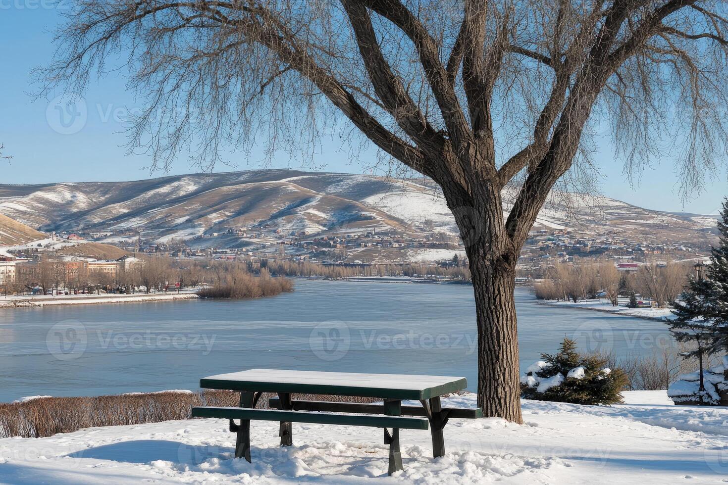 Snowy picnic table overlooking winter river and mountains photo