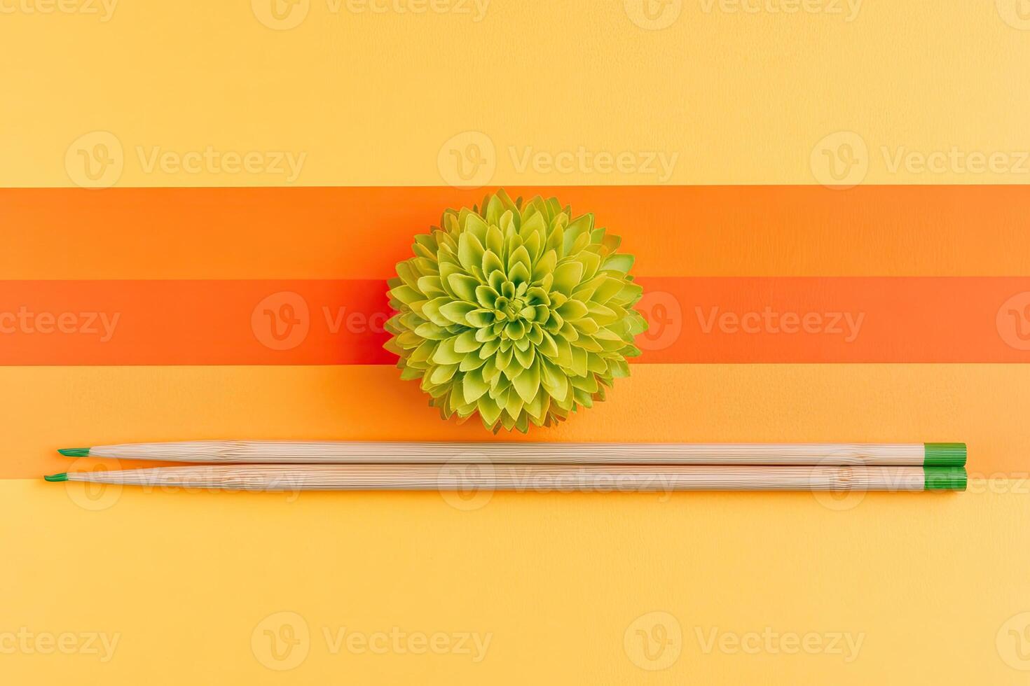 A green flower and two chopsticks on a yellow and orange striped background photo