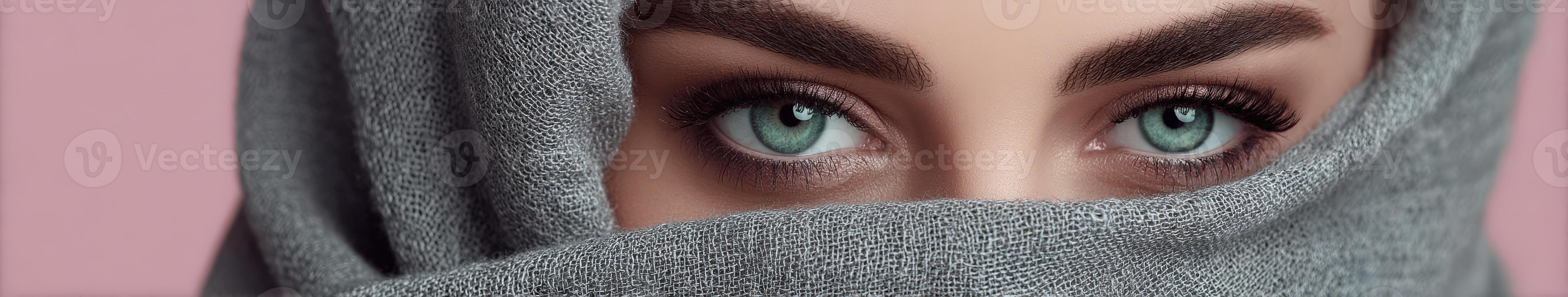 Close-up of striking eyes behind a grey scarf in soft lighting photo