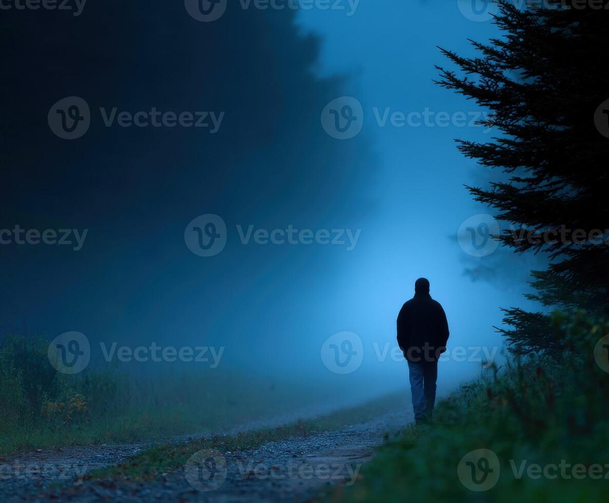 Mysterious figure walking along a foggy forest path during twilight photo