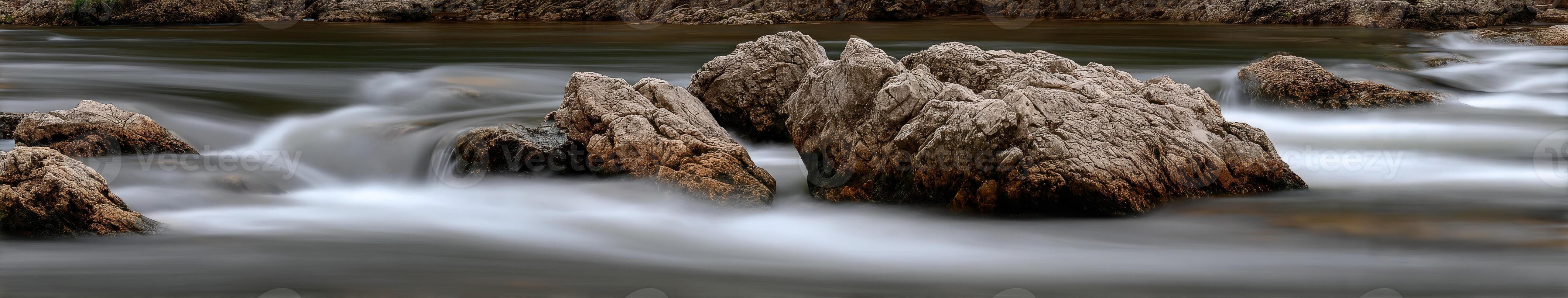 Smooth flowing water rushes around large rocks in mountain river photo